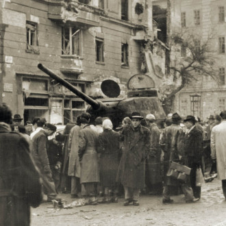Járókelők egy kilőtt szovjet harckocsi körül egy budapesti utcán, 1956-ban.