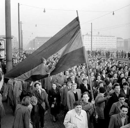 Tömeg vonul 1956 októberében, középen a kivágott címerű, lyukas magyar zászlóval.